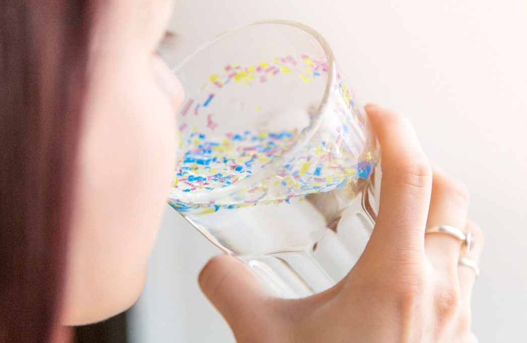 woman drinking a glass of water containing microplastics on the surface